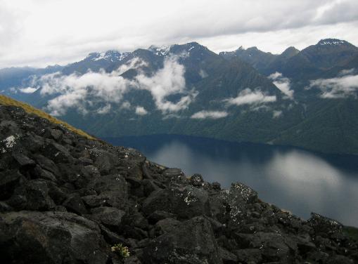 Charcoal boulders contrast with the soft blue lake and misty mountains