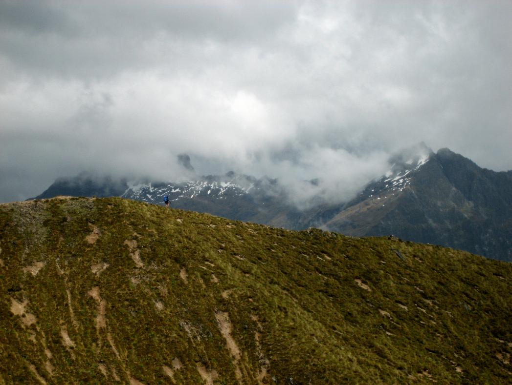 A lone hiker crosses the ridge with mists billowing around the mountains